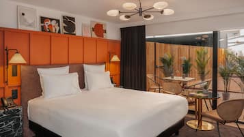 A hotel room with a large bed, two bedside lamps, a wooden headboard, a small table with chairs, and a view of the outdoors.