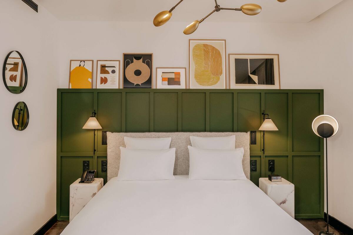 A neatly arranged hotel room with a green headboard, a large bed, two bedside tables with lamps, and a ceiling light fixture.