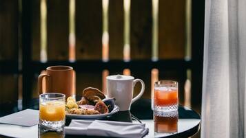 A breakfast table with a mug, juice, and a glass of orange juice on a balcony with a view of buildings.