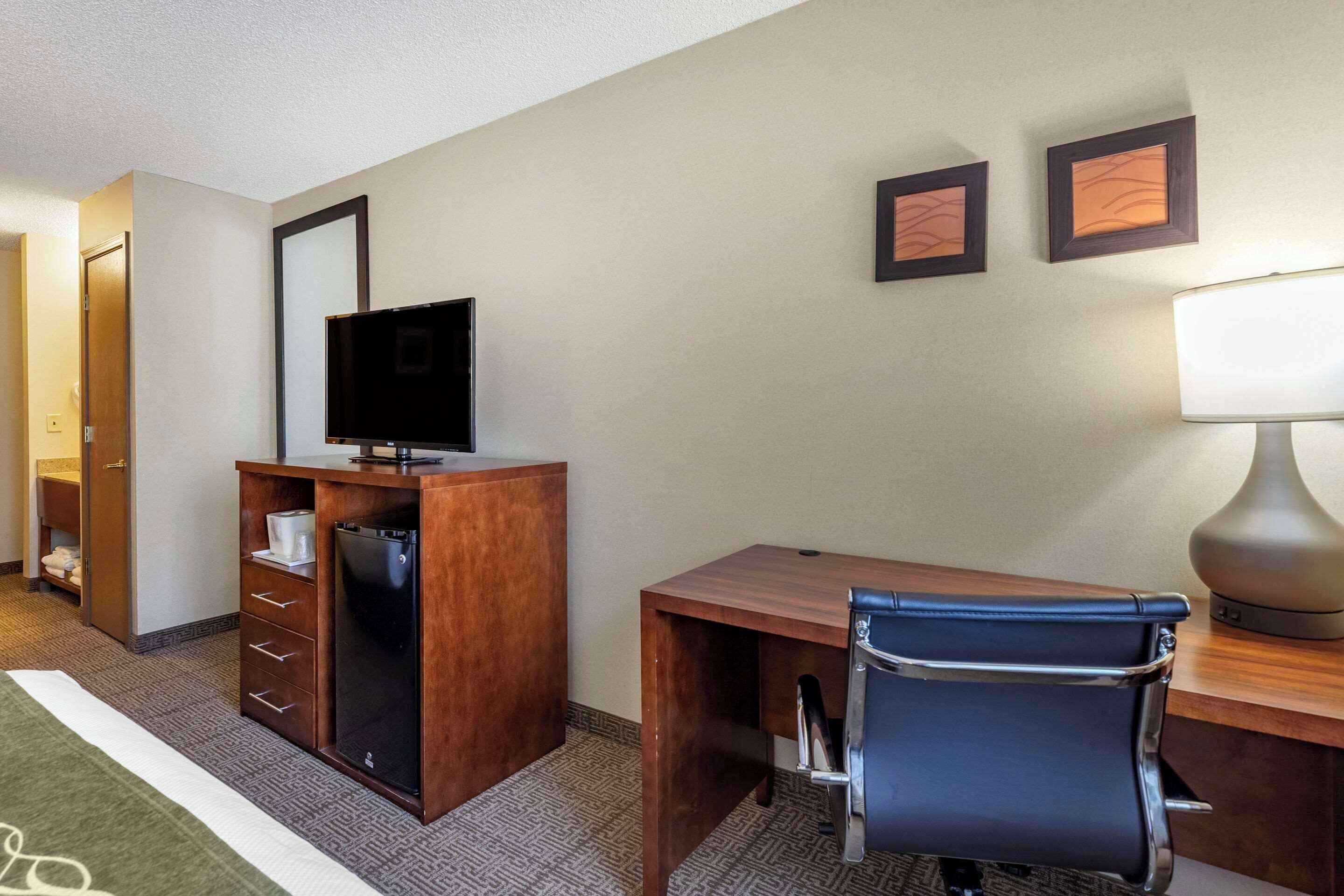 Een hotelkamer met een houten bureau, een zwarte lederen fauteuil, een televisie en een lamp.
