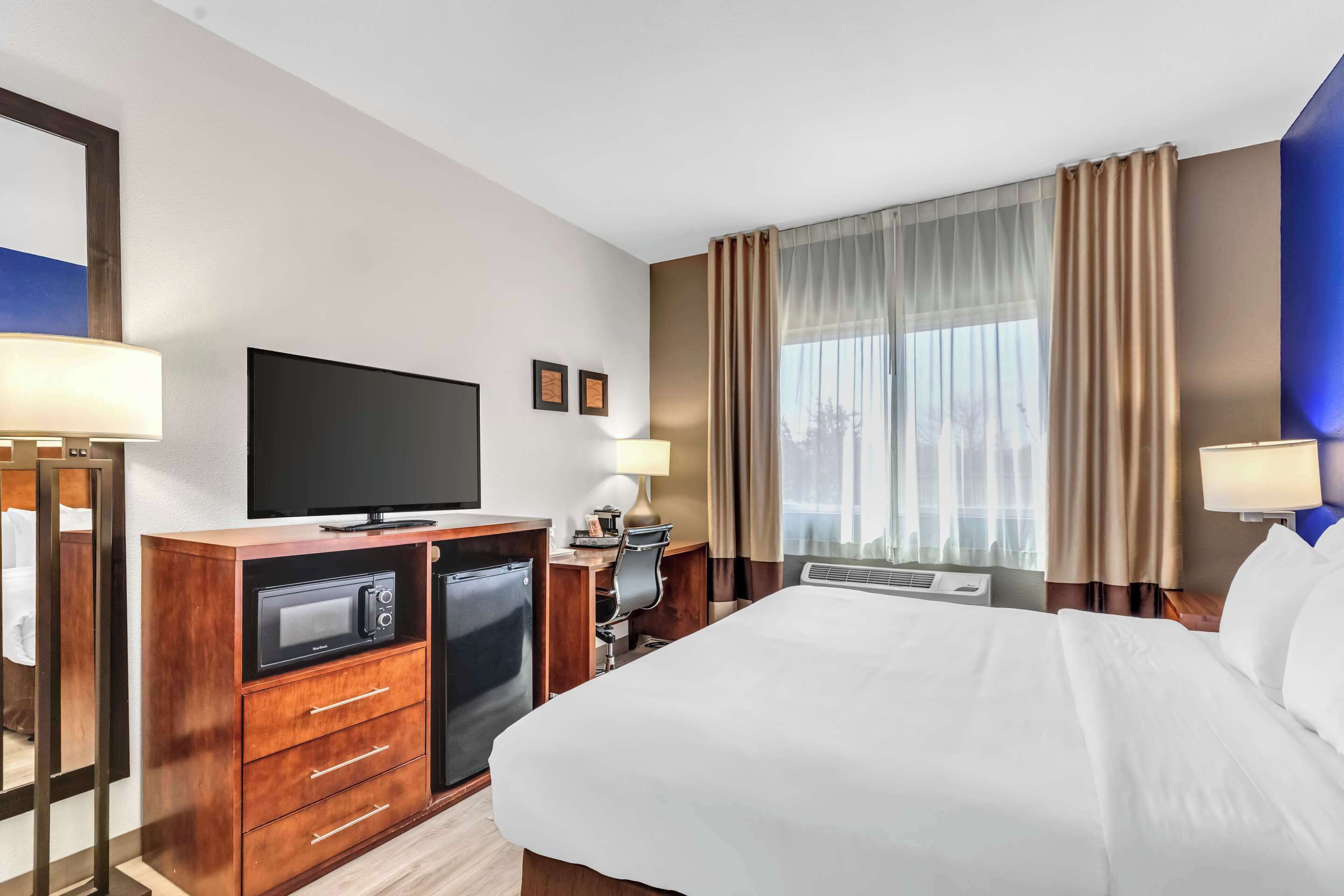 A hotel room with a bed, a TV, a desk with a computer, a microwave, and a mini-fridge.