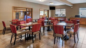 A dining area with multiple tables and chairs, a kitchen area, and a television mounted on the wall.