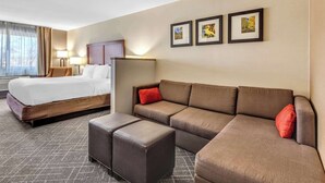 A hotel room with a bed, a sofa, an ottoman, and a wall with framed pictures. - Comfort Inn Denver West Arvada Station (Wheat Ridge)