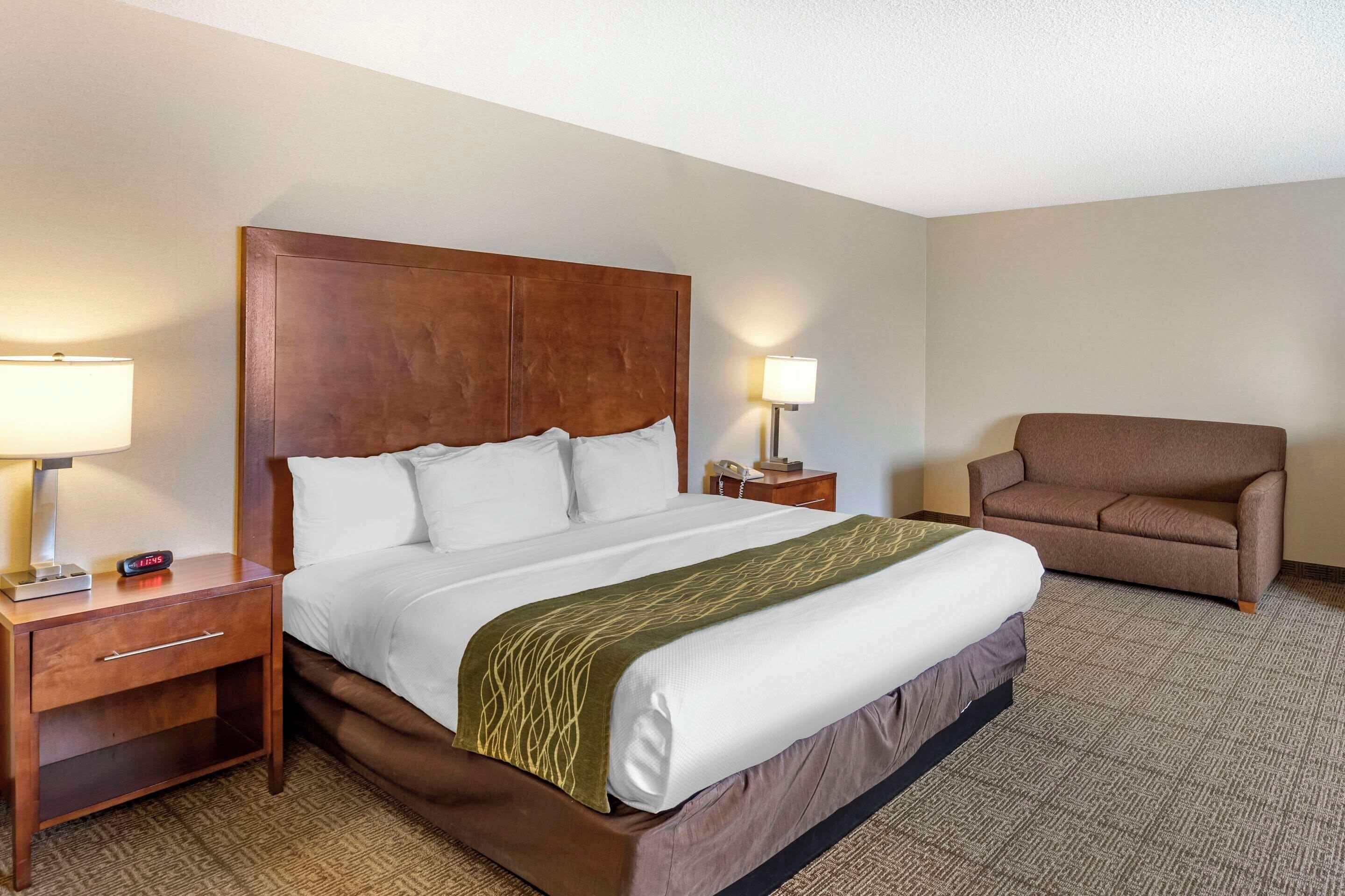 A hotel room with a large bed, a nightstand with a lamp, a chair, and a bedside table with a phone.
