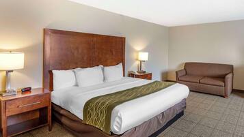 A hotel room with a large bed, a nightstand with a lamp, a chair, and a bedside table with a phone.