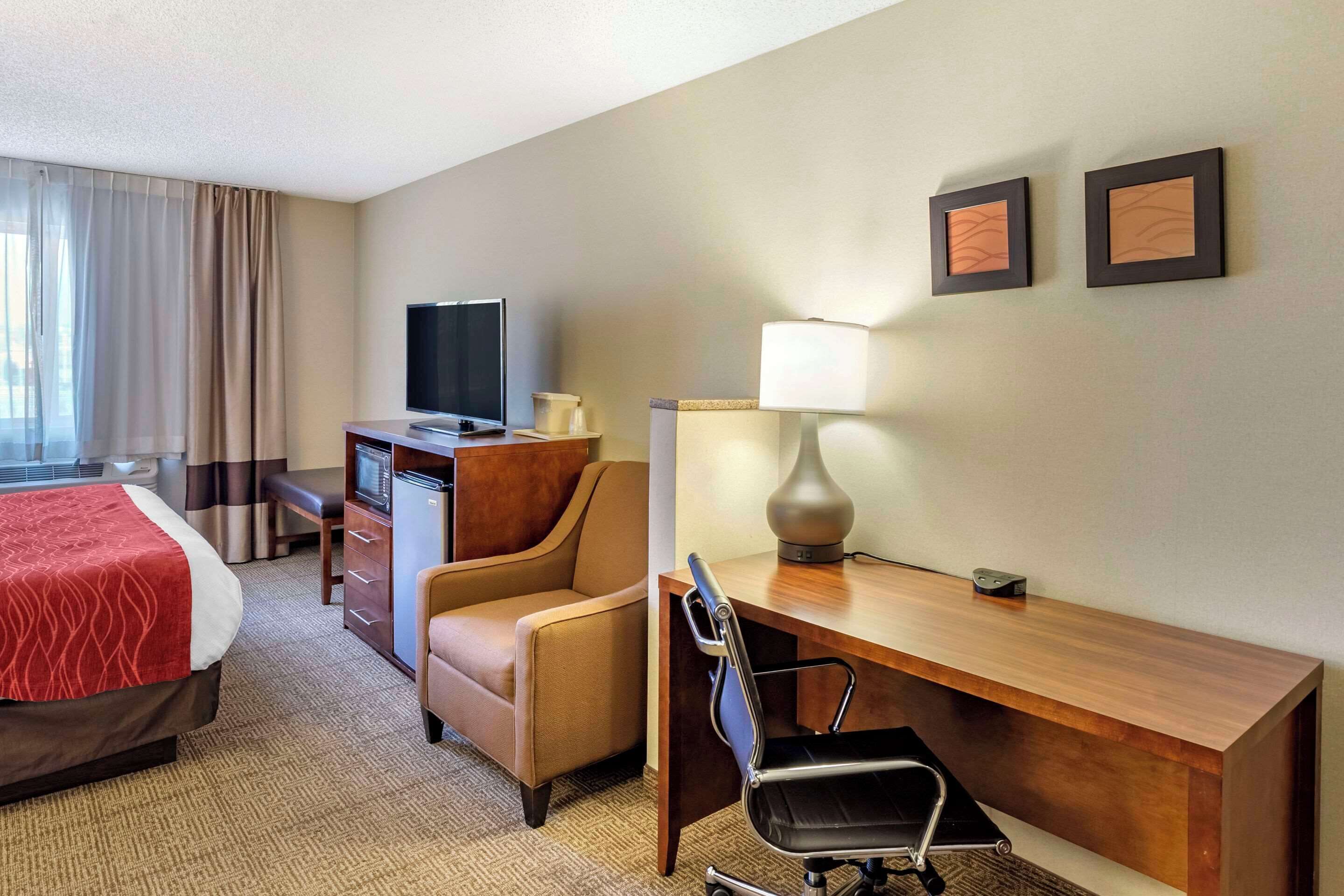 A hotel room with a bed, a desk with a lamp, a chair, a television, and a small refrigerator.