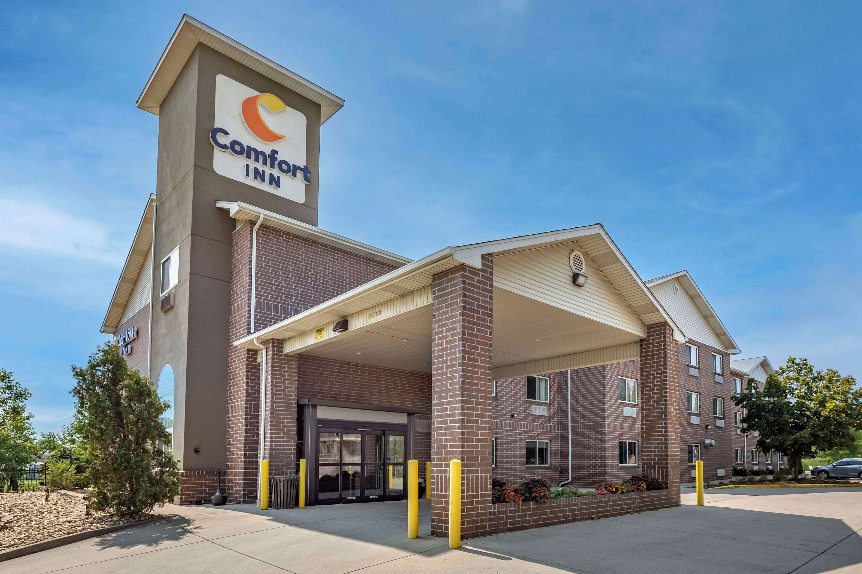 Un hôtel Comfort Inn avec une façade en briques, une entrée abritée et un ciel dégagé.