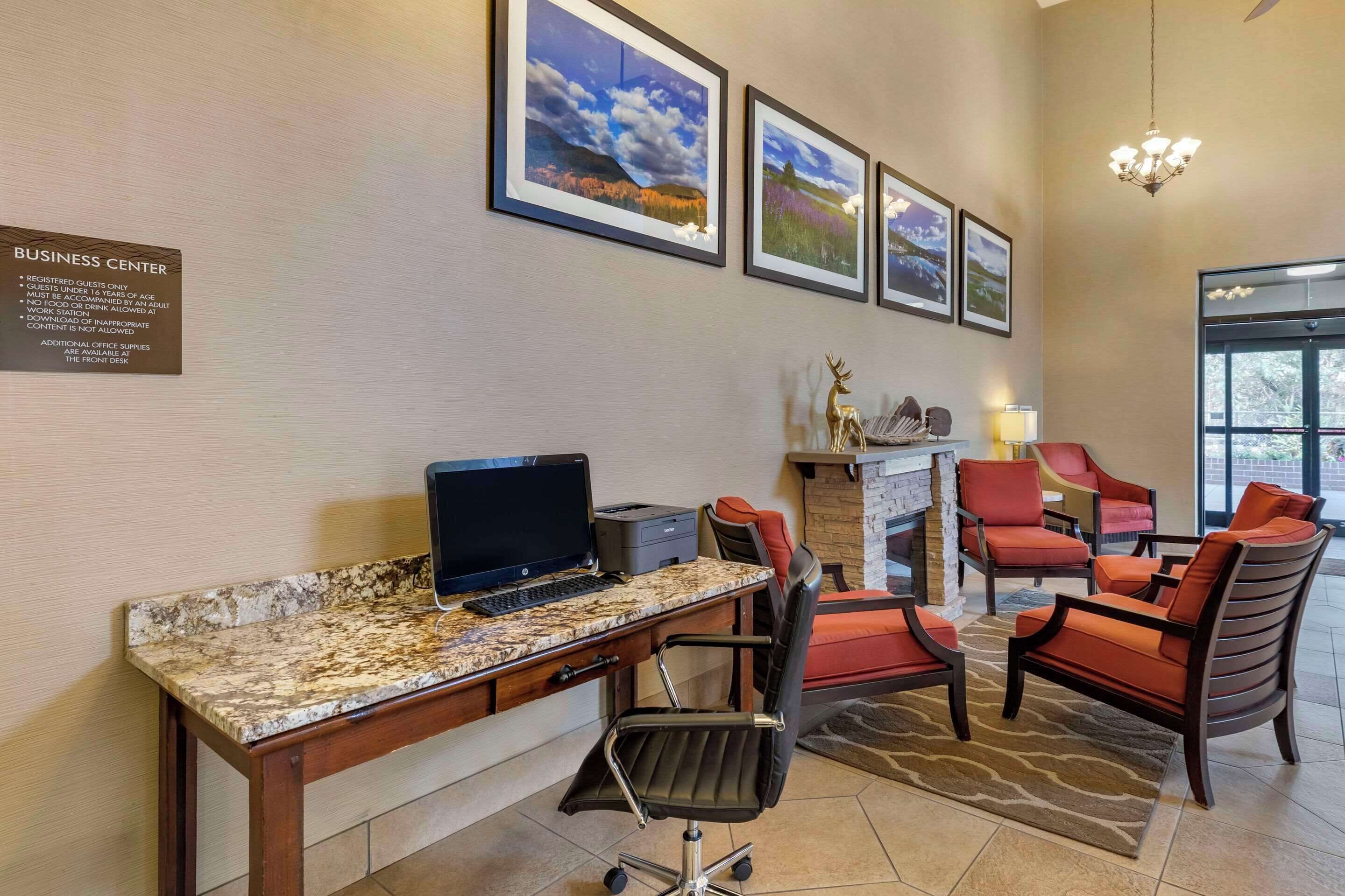A business center with a desktop computer, office chairs, a fireplace, and framed pictures on the wall.