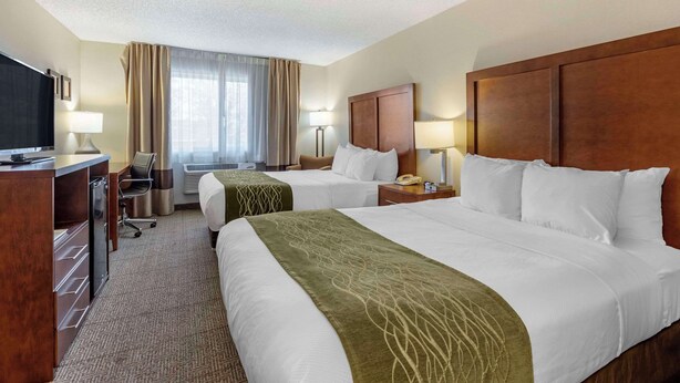 A hotel room with two beds, a desk with a television, and a window with curtains.