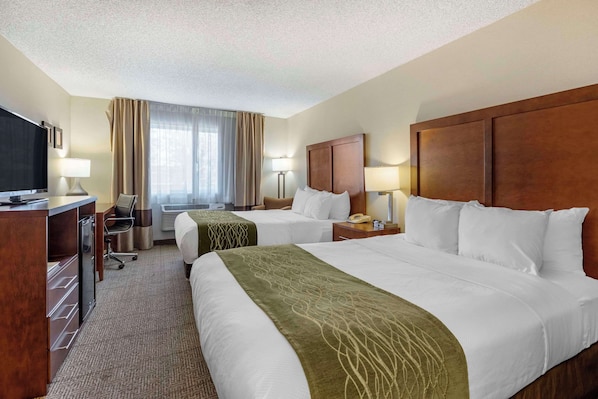 A hotel room with two beds, a desk with a television, and a window with curtains.