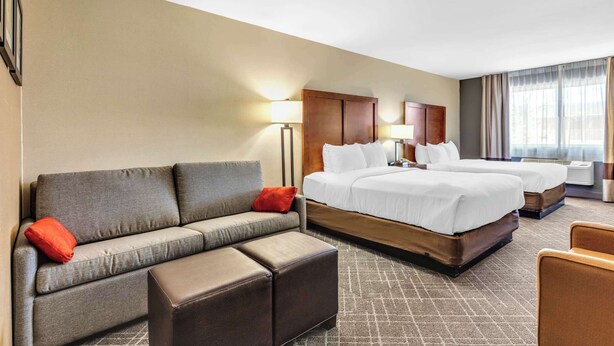 A hotel room with a sofa, two beds, a small table, and a window with curtains. - Comfort Inn Denver West Arvada Station (Wheat Ridge)