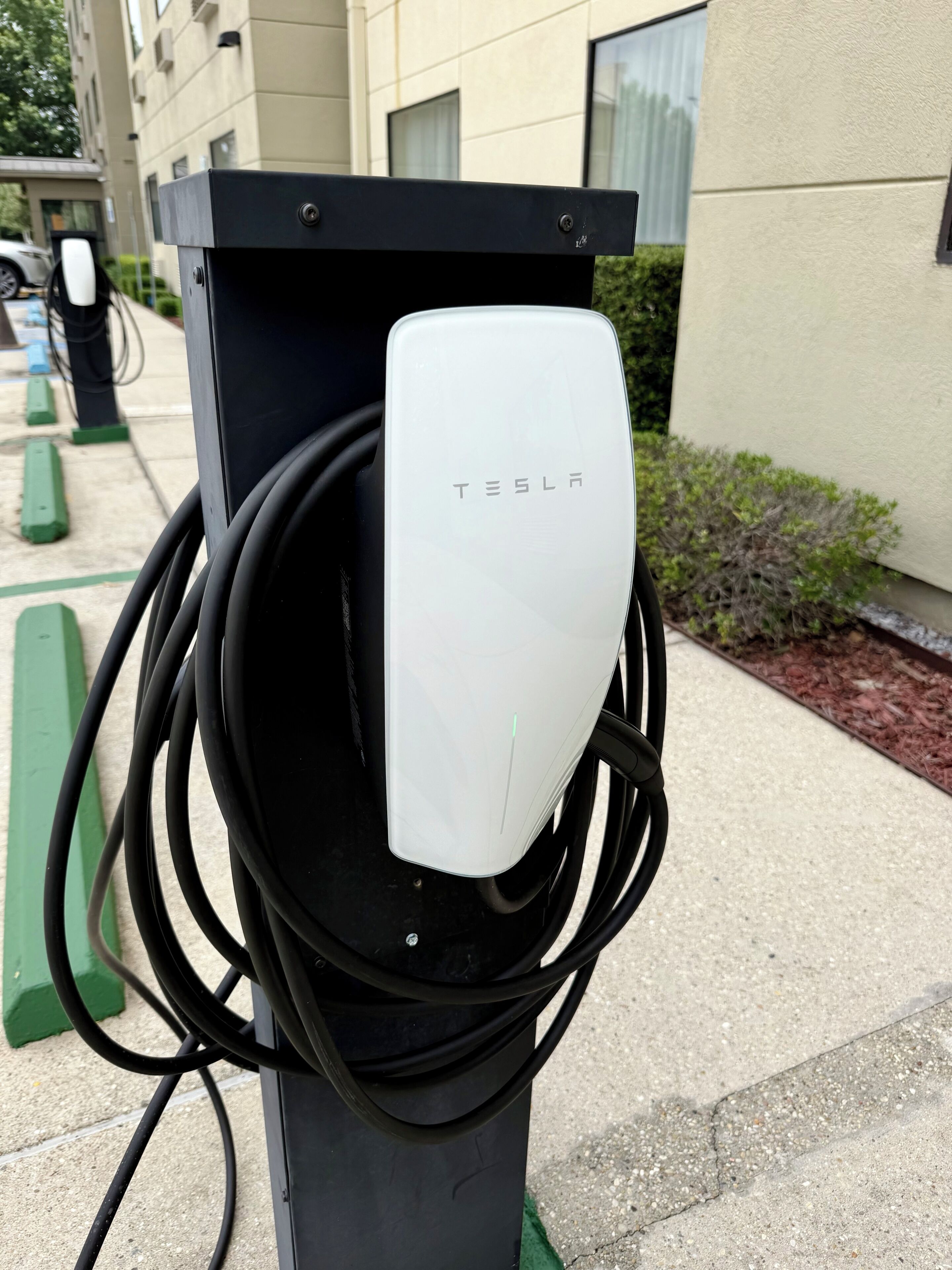 A Tesla charging station with a white charging unit and black cables.