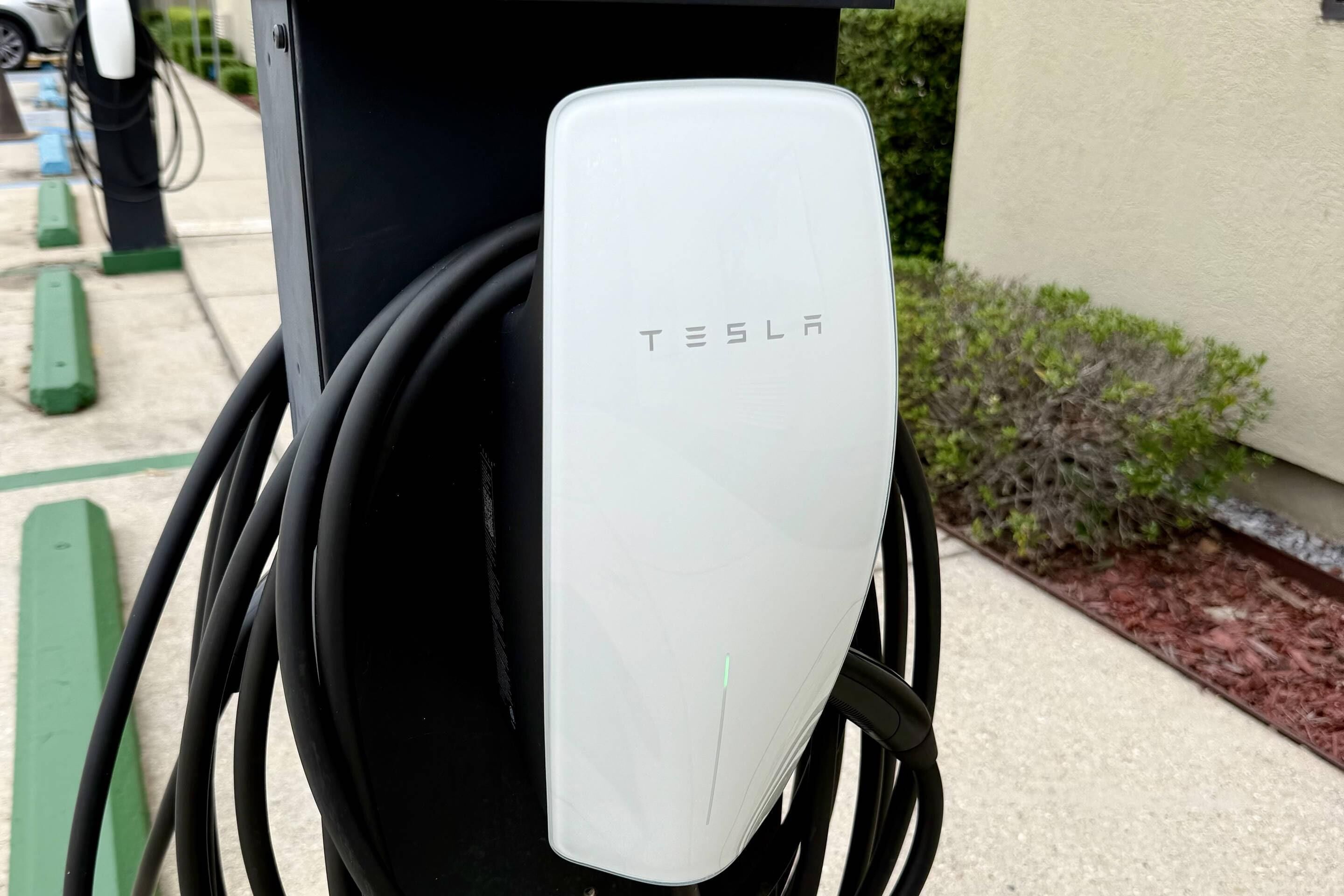 Une borne de recharge Tesla dotée d’un appareil de recharge blanc et de câbles noirs.