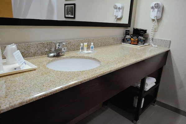 A hotel bathroom with a granite countertop sink, a mirror, a hairdryer, and a phone on the wall.