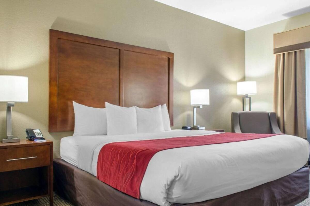 Une chambre d’hôtel avec un grand lit, deux tables de chevet, une chaise et une fenêtre avec des rideaux.