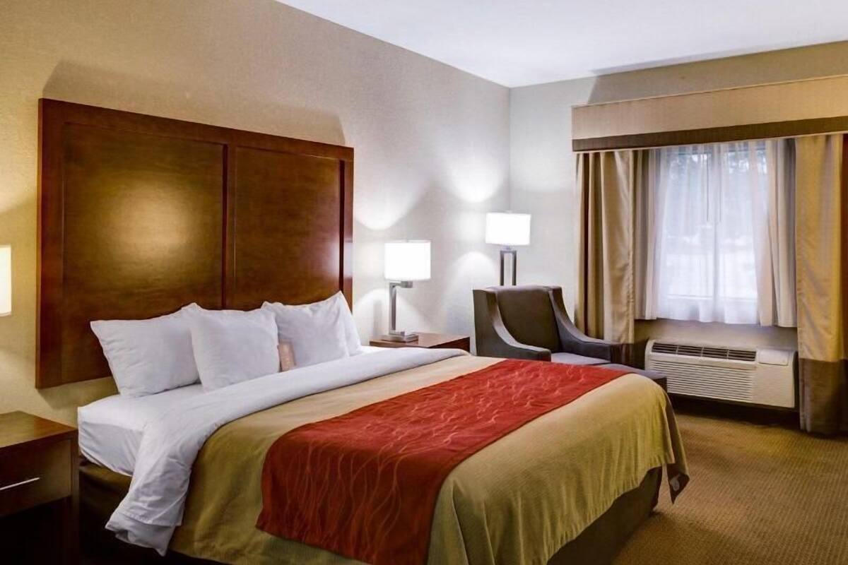 Une chambre d’hôtel avec un lit, des tables de chevet, une chaise, une lampe et une fenêtre avec des rideaux.