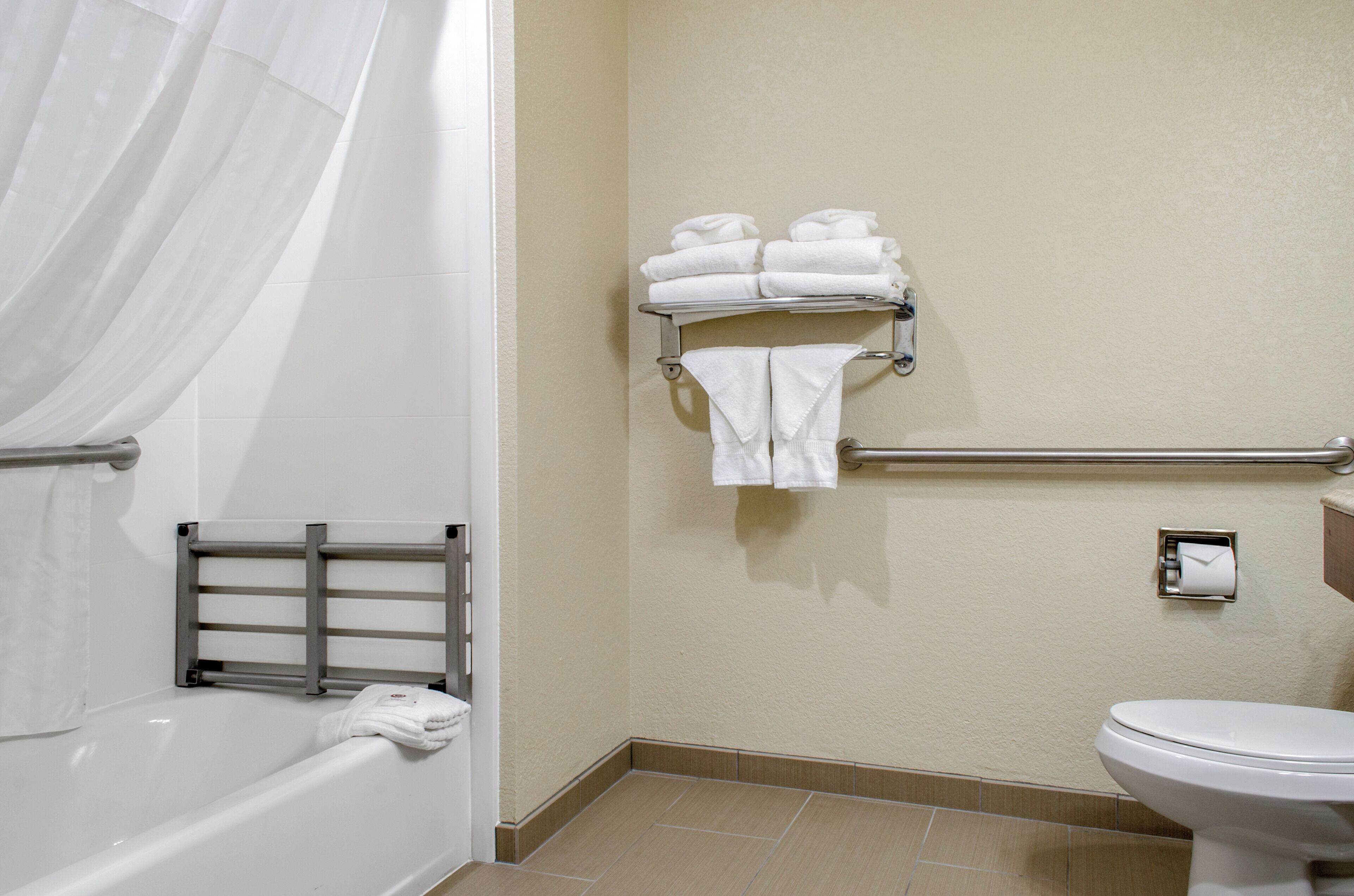 Un baño con bañera, inodoro, toallero con toallas dobladas y barra de apoyo.