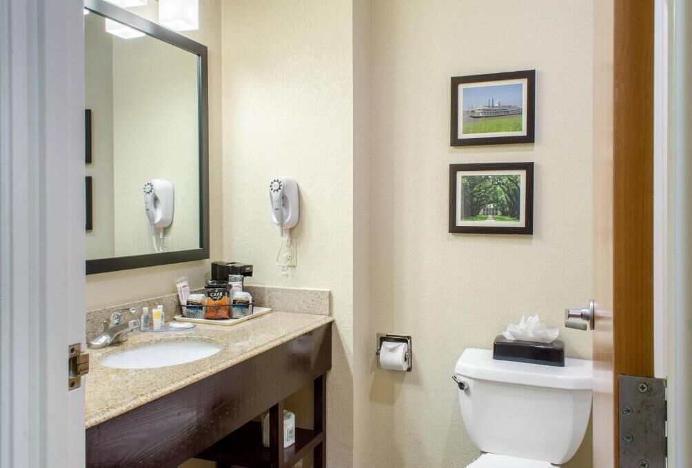 Un baño con lavabo, espejo, dispensador de toallas y retrete. Hay dos cuadros enmarcados en la pared.