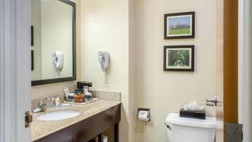 Un baño con lavabo, espejo, dispensador de toallas y retrete. Hay dos cuadros enmarcados en la pared.