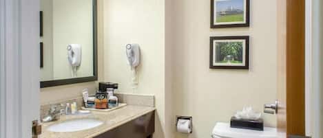 Un baño con lavabo, espejo, dispensador de toallas y retrete. Hay dos cuadros enmarcados en la pared.