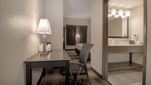 A hotel room with a desk, chair, lamp, bed, curtains, and a bathroom with a mirror and sink. - Quality Inn Roseville-Detroit North (Roseville)
