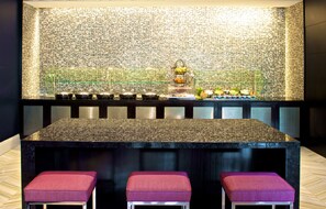 A bar area with a mosaic tile backsplash, a granite countertop, and three red cushioned stools. - Beverly Hills Marriott (Los Angeles)