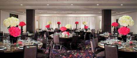 Un salón de banquetes con mesas redondas dispuestas para comer, cada una con un centro de mesa floral.