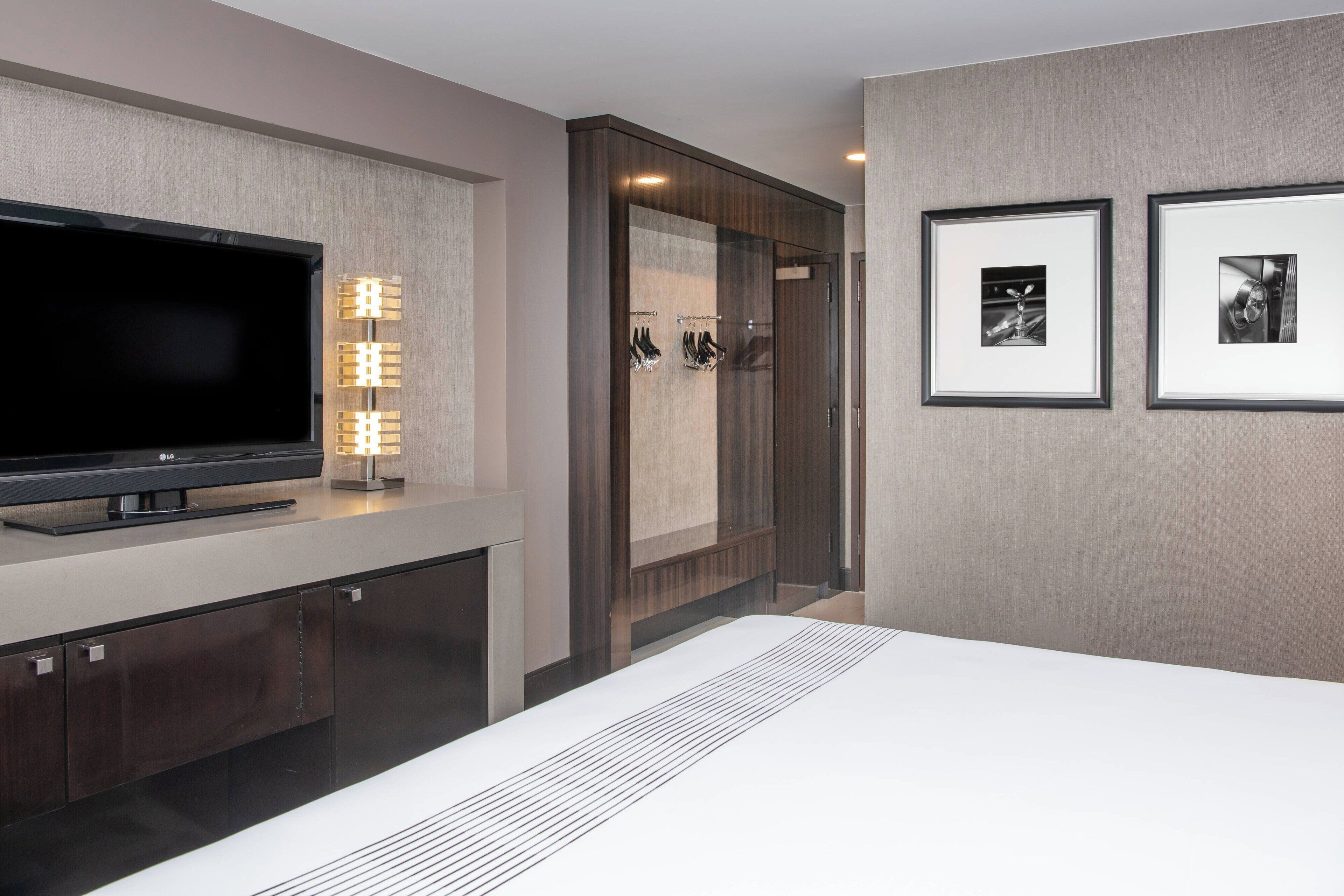 A modern hotel room with a flat-screen TV, a vanity with a mirror, and framed pictures on the wall.