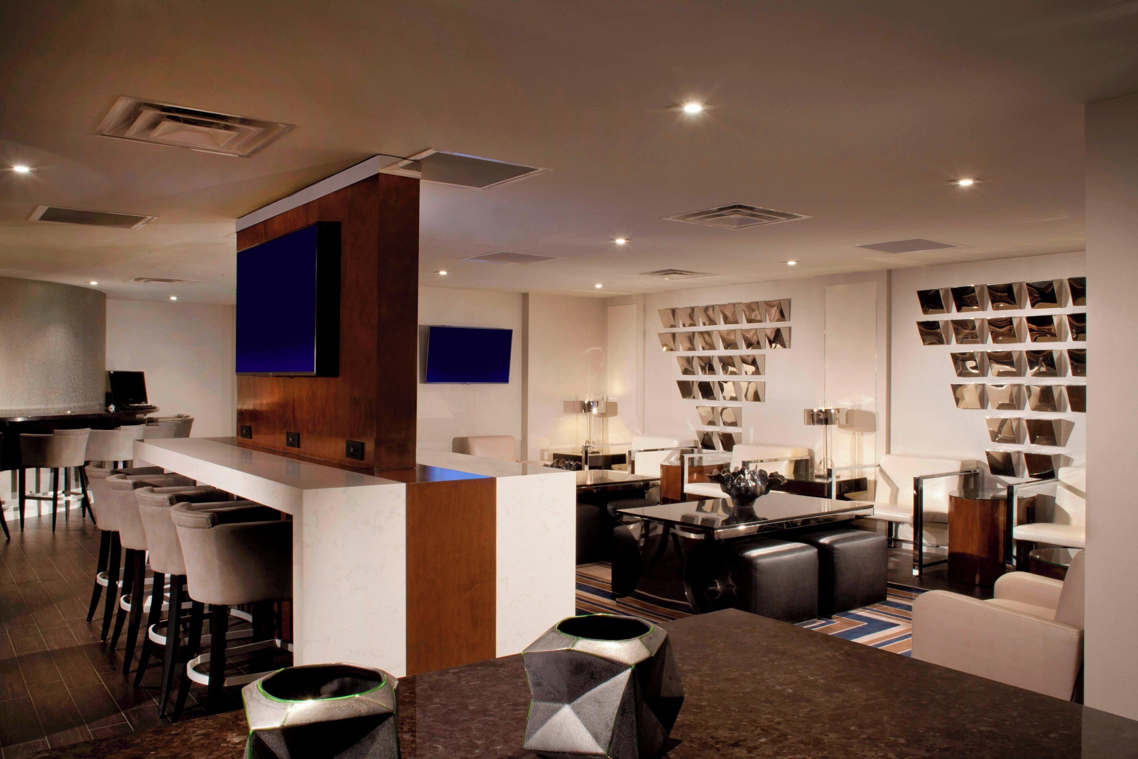 Un moderno vestíbulo de hotel con zona de bar, asientos y una pared de fotografías enmarcadas.