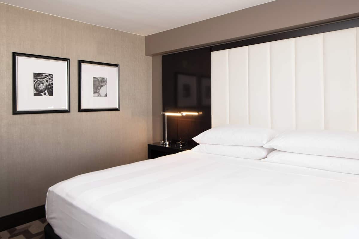A hotel room with a large bed, two framed pictures on the wall, and a nightstand with a lamp.
