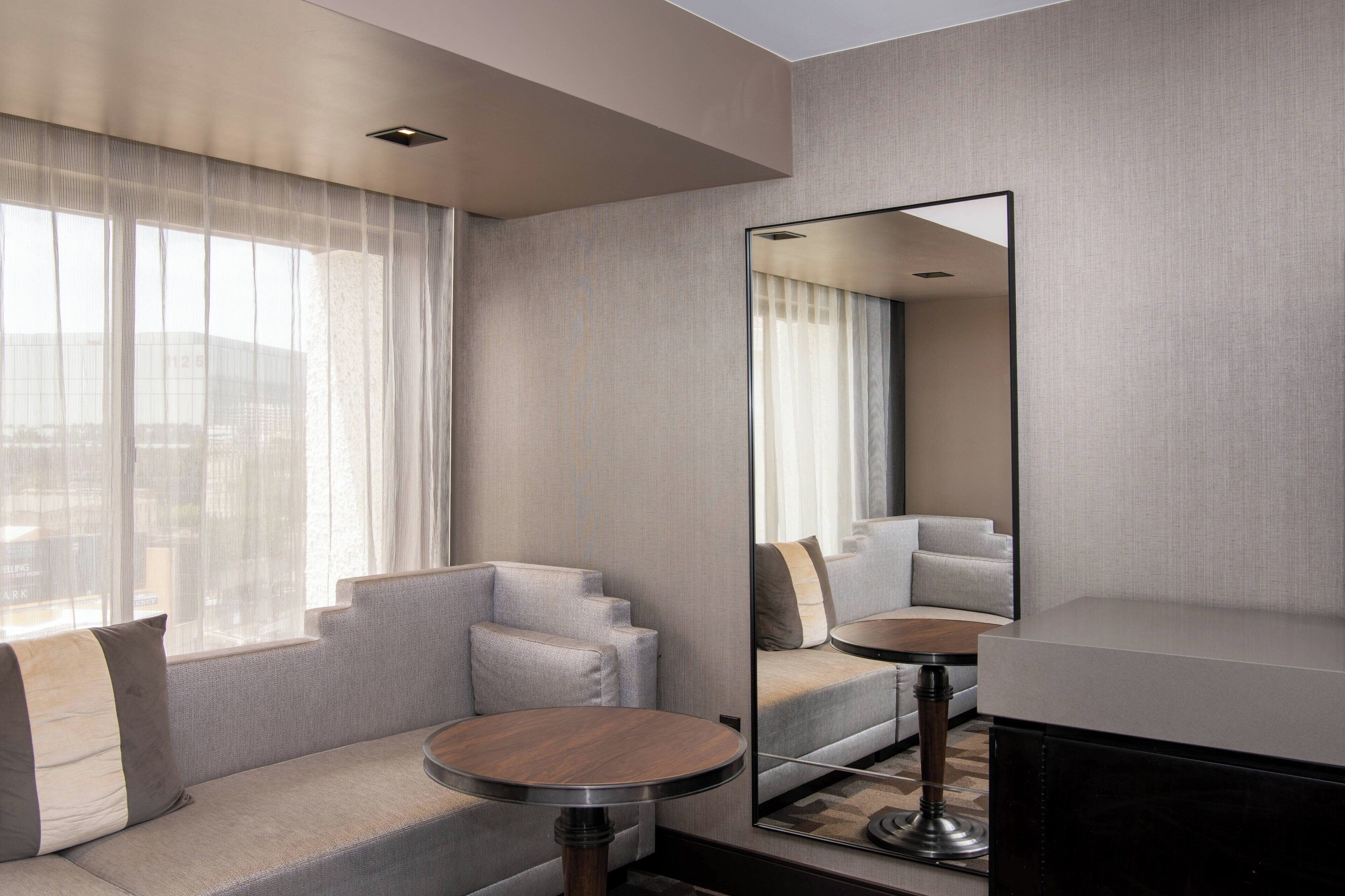 A modern hotel room with a sofa, a round table, and a large mirror.