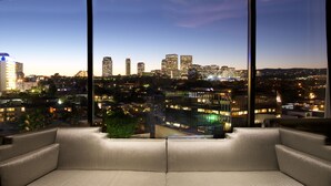 Sala de estar moderna com vista para a cidade, com um sofá e uma pequena planta.