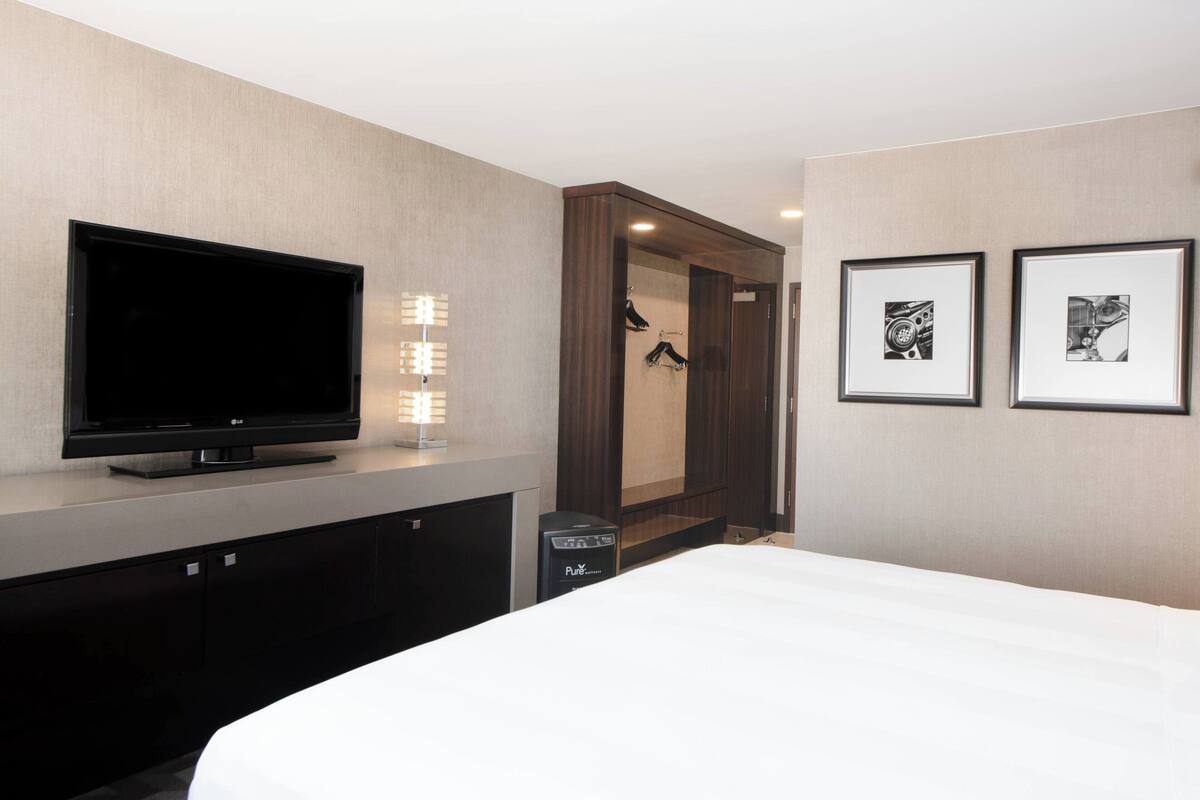 A hotel room with a flat-screen TV, a vanity with a mirror, and two framed pictures on the wall.