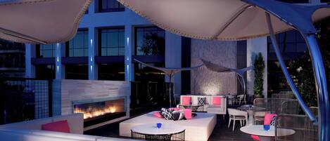 An outdoor seating area with cushioned sofas, round tables, and umbrellas providing shade.