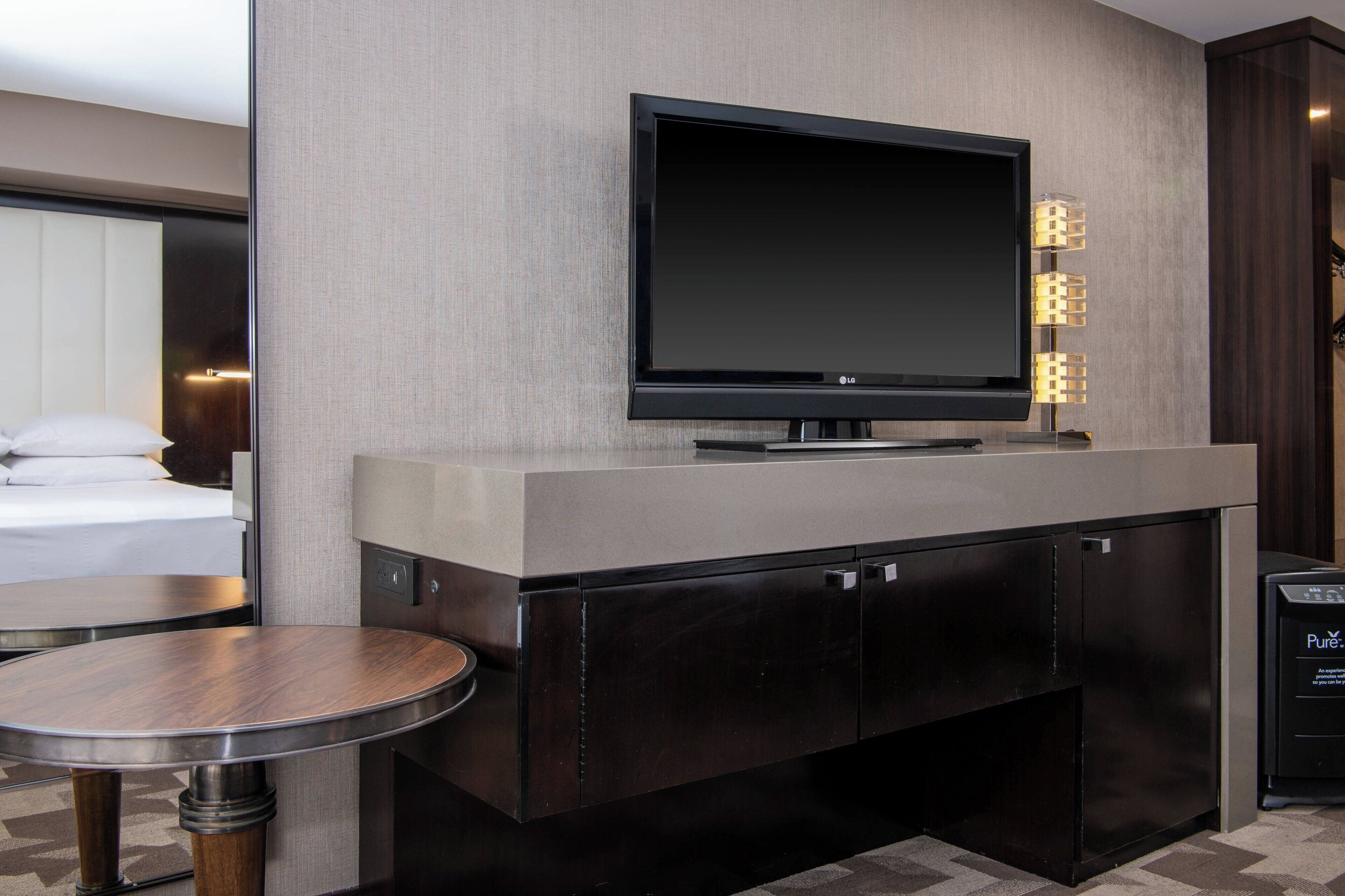 A modern hotel room with a flat-screen TV mounted on a wall, a small round table, and a built-in cabinet.