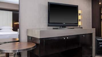 A modern hotel room with a flat-screen TV mounted on a wall, a small round table, and a built-in cabinet.