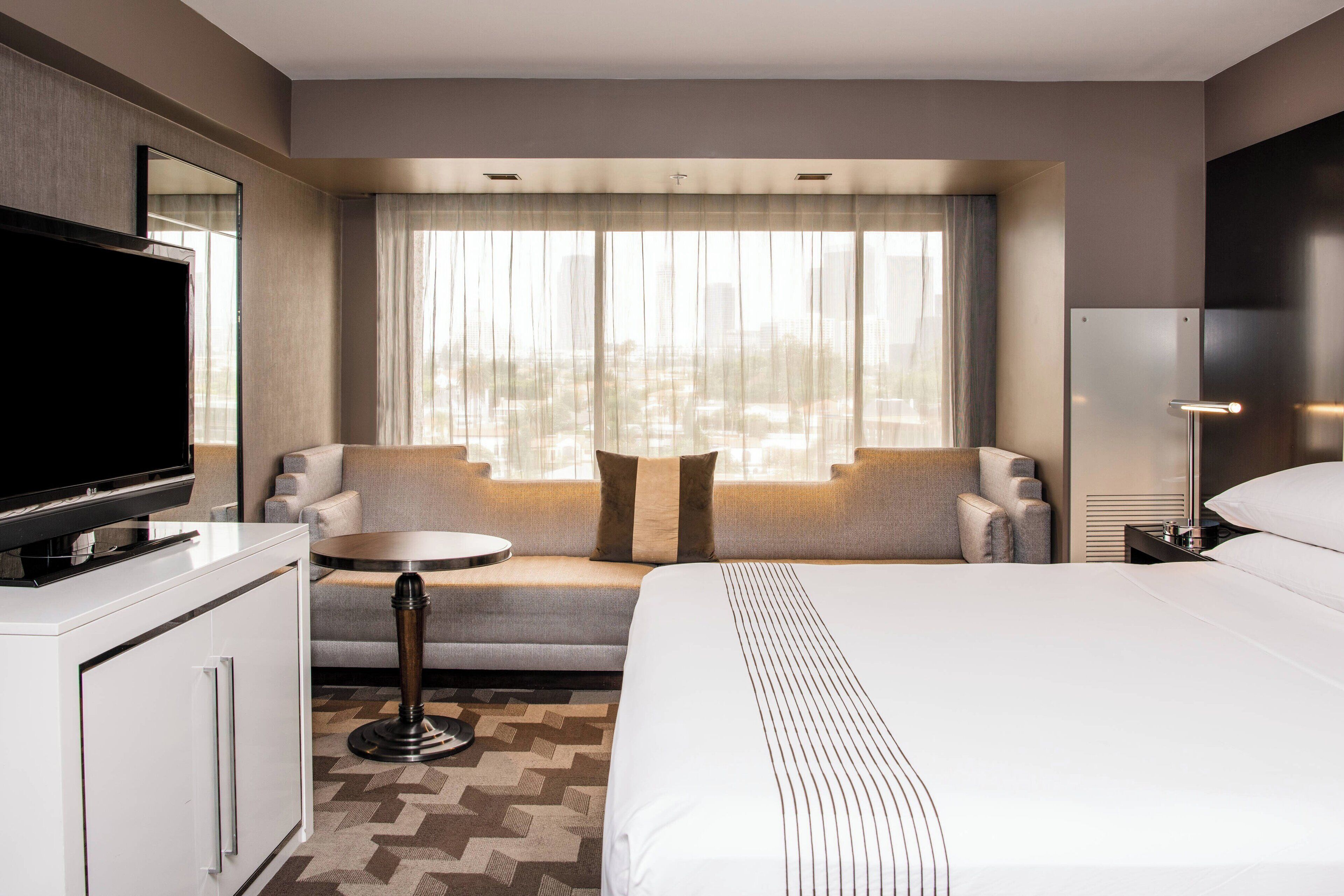 A hotel room with a large bed, a sofa, a TV, a desk, and a window with curtains.