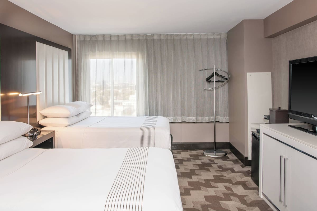 A hotel room with two beds, a TV, a desk, and a window with curtains.