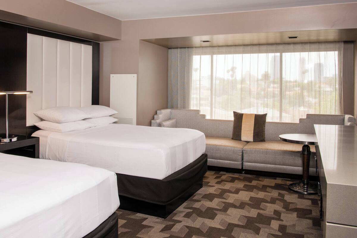 A hotel room with two beds, a sofa, a small table, and a window with curtains.