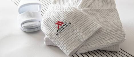 A neatly folded white robe with a logo and text, and a pair of white slippers on a striped surface.