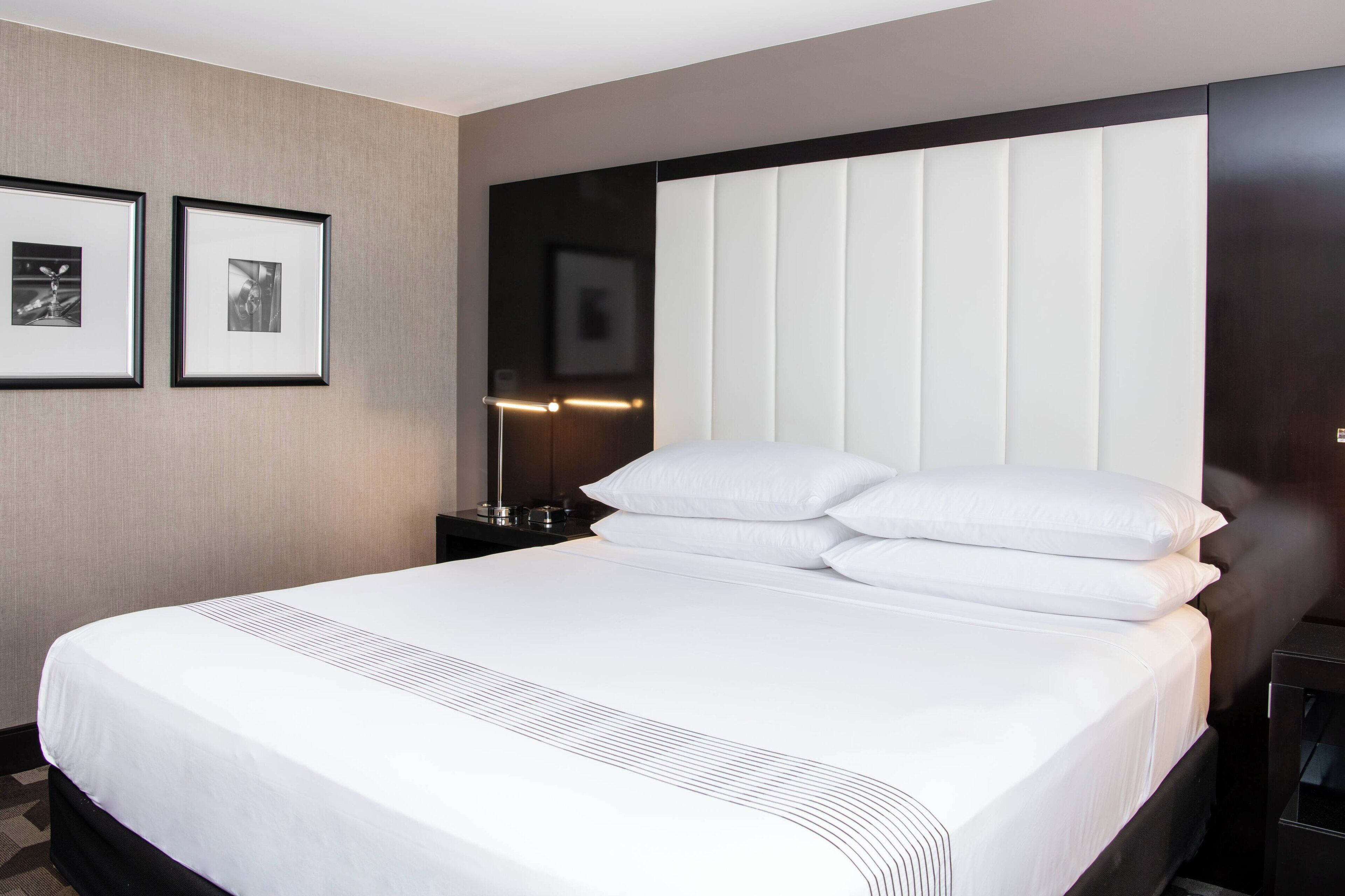 Habitación de hotel con una cama grande, cabecero con listones verticales, dos cuadros en la pared y una mesita de noche con lámpara.