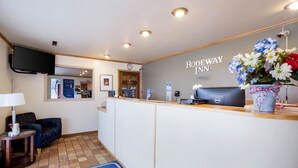Un espace d’accueil comprenant un comptoir, une horloge, un téléviseur à écran plat, un arrangement floral et un panneau indiquant « RODEWAY INN ».