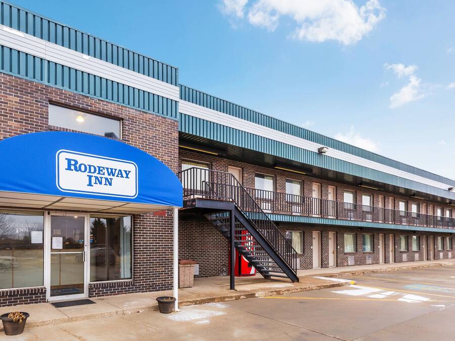 A Rodeway Inn building with a blue awning, brick facade, and a staircase leading to an upper level.