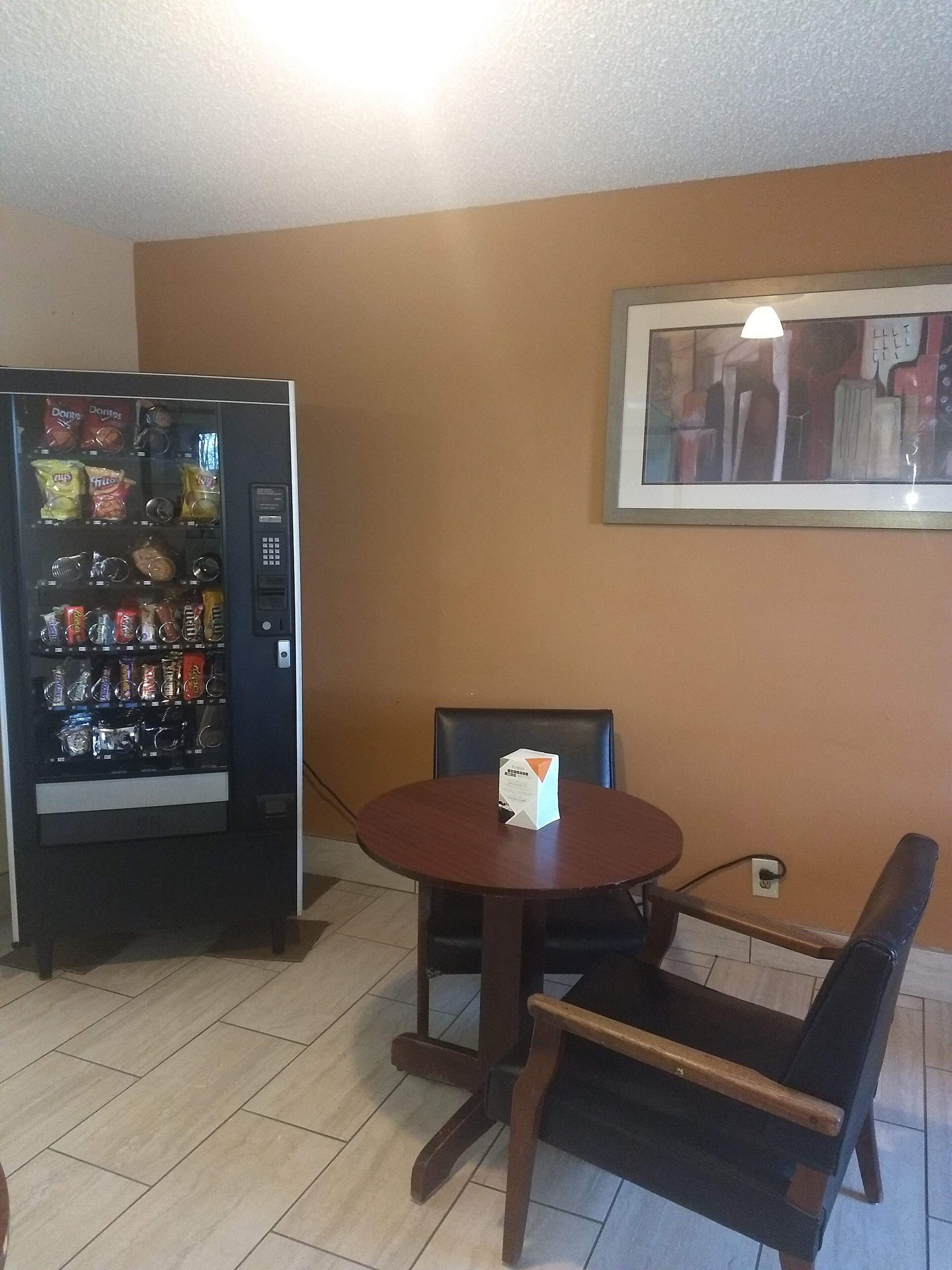 A dining area with a table and chairs, a vending machine, and a framed picture on the wall.