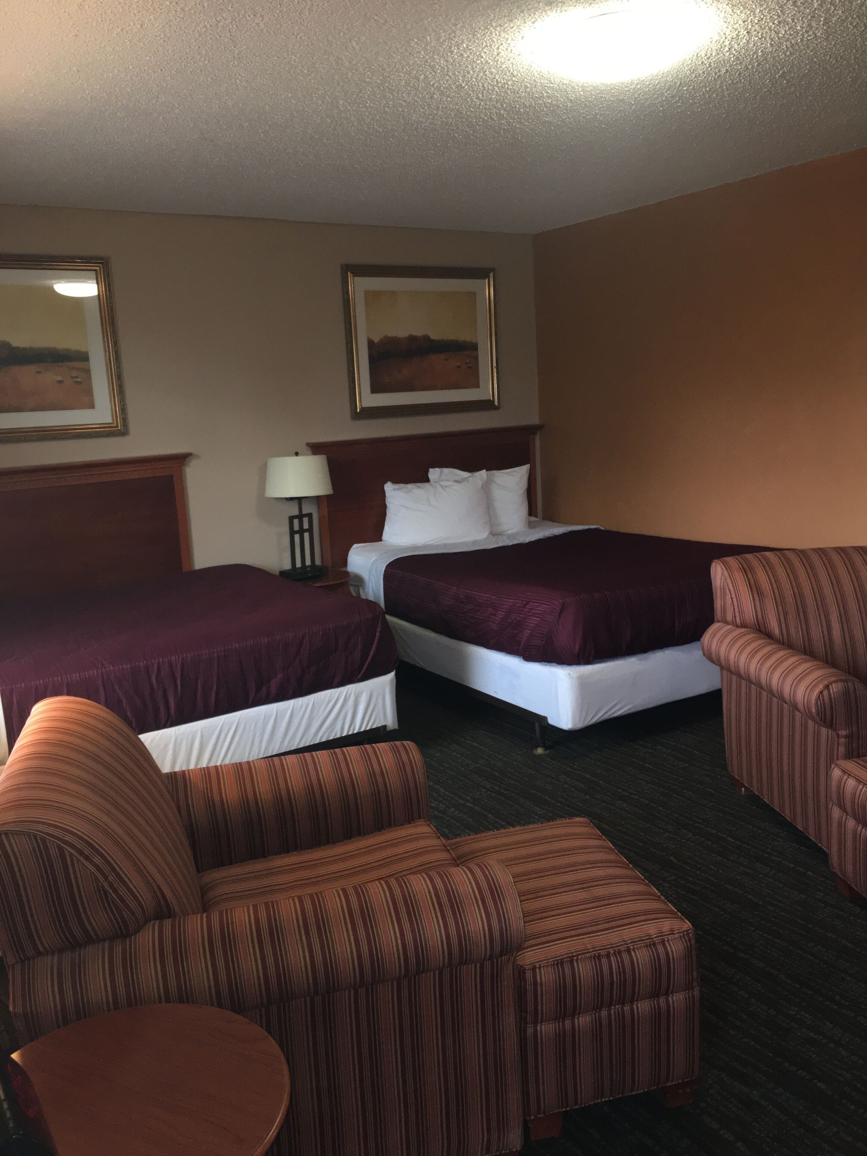 A hotel room with two beds, a nightstand, a lamp, and striped furniture.