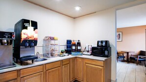 Une cuisine moderne équipée d’un distributeur de jus de fruits, d’une machine à café, d’un four à micro-ondes et d’un espace dédié à la préparation du café.