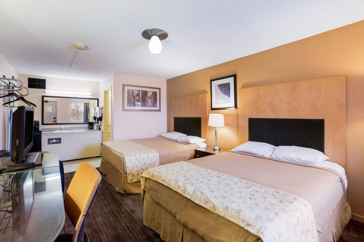 Una habitación de hotel con dos camas, un escritorio, un espejo, un televisor y una kitchenette.