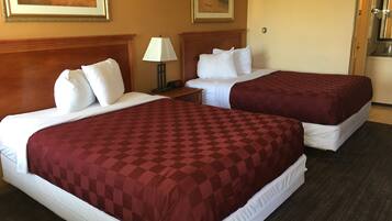 A hotel room with two beds, each with a red checkered bedspread and white pillows. There is a nightstand with a lamp between the beds, and a painting on the wall above the nightstand.