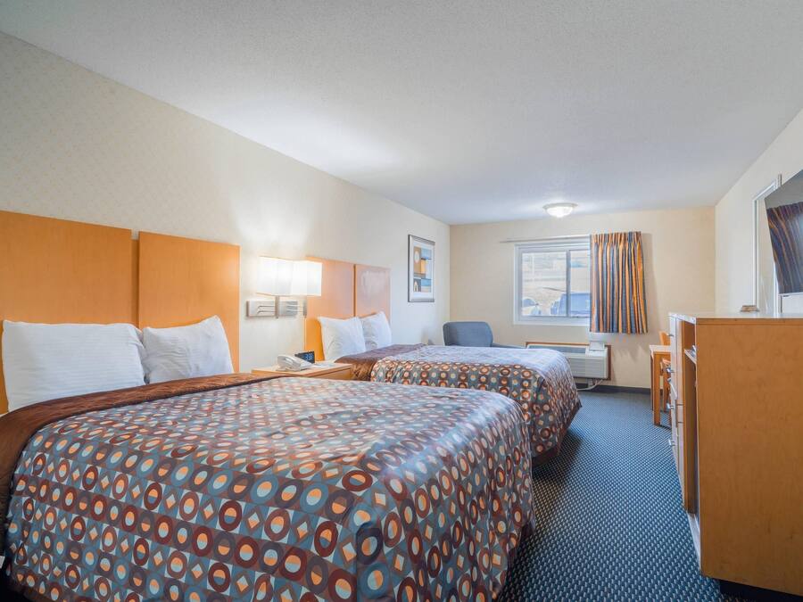 A hotel room with two beds, a desk, a chair, a TV, and a window with curtains.