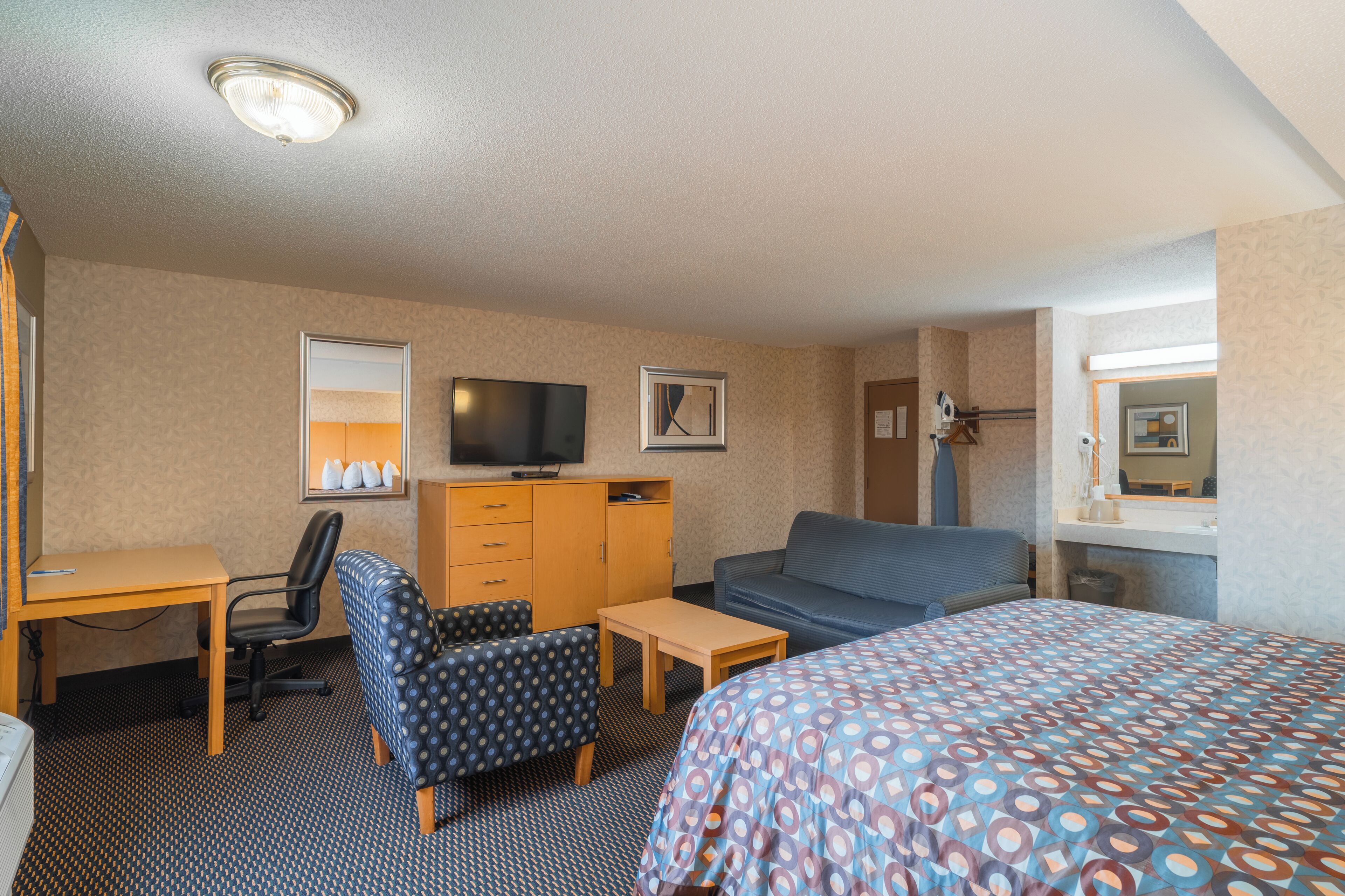 Ein Hotelzimmer mit einem Bett, einem Schreibtisch, einem Stuhl, einer Couch, einem Fernseher und einem Spiegel.